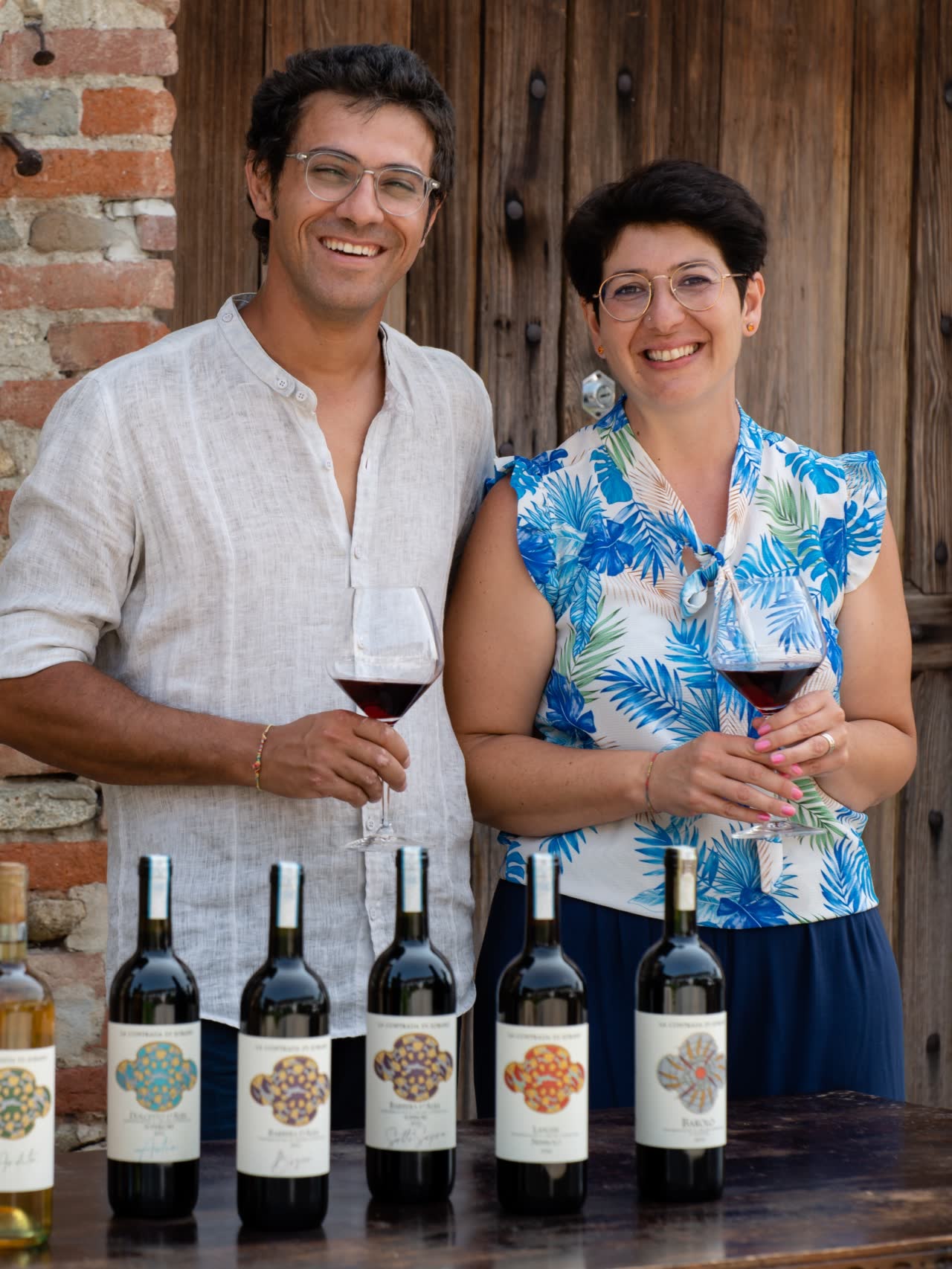 Paolo e Cristina Baudano in posa con calici e bottiglie di vino rosso